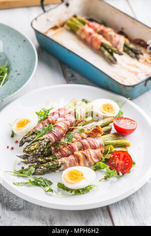 Frischer Spargel in Schinken auf einem weißen Teller mit Rucola Tomaten und Eier gewickelt. Stockfoto