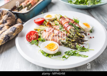 Frischer Spargel in Schinken auf einem weißen Teller mit Rucola Tomaten und Eier gewickelt. Stockfoto