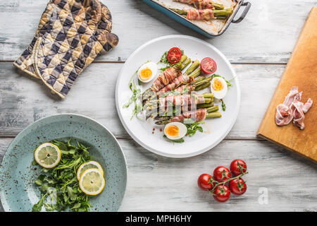 Frischer Spargel in Schinken auf einem weißen Teller mit Rucola Tomaten und Eier aufgewickelt oben auf Ansicht. Stockfoto