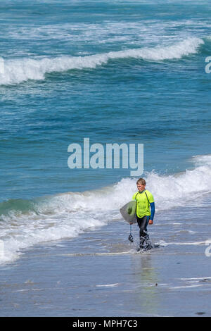 Ein junger Surfer sein Surfbrett tragen und wandern entlang der Küstenlinie an Sennen Cove in Cornwall. Stockfoto