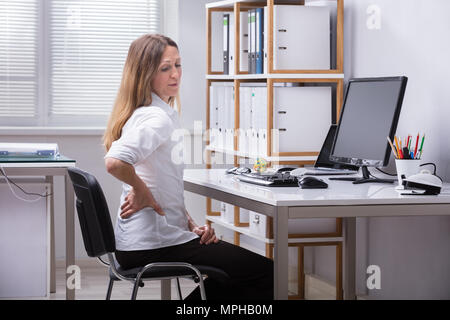 Seitenansicht eines reifen Geschäftsfrau Sitzen auf Stuhl Rückenschmerzen leiden. Stockfoto