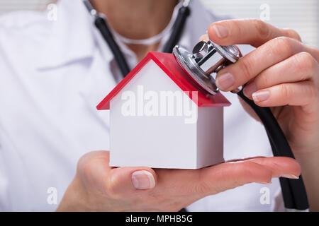 Nahaufnahme von einem Arzt prüfen Einfache Modell Haus mit Stethoskop Stockfoto