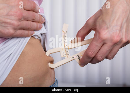 Nahaufnahme von einer Frau Hand messen Bauch Fett mit Bremssattel Stockfoto