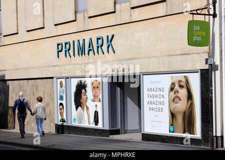 Paar mittleren Alters zu Fuß vorbei an der Außenseite des Primark, Cheltenham, Gloucestershire. Job Center Plus Zeichen in der oberen rechten Ecke. Stockfoto