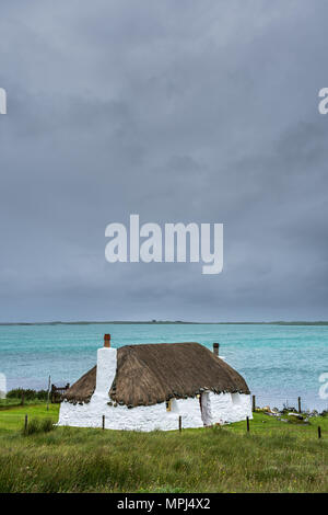 Traditionell White Cottage mit Strohdach, in der Nähe der türkisfarbenen Bucht, mit Oben stürmische bewölkt dunklen Himmel. Insel North Uist, Schottland. Stockfoto