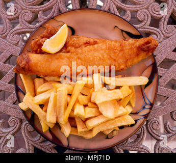 Fisch und Chips essen mit einer Zitrone Keil oder Keil der Zitrone auf einem Tisch im Freien. Stockfoto