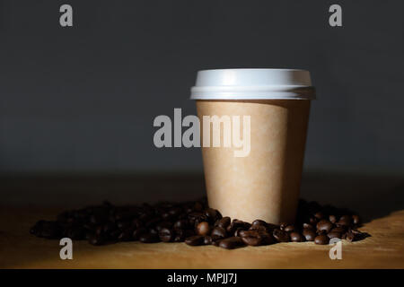 Verfügbare Tasse Kaffee neben einigen gerösteten Kaffeebohnen auf einem Holztisch recycelt. Schwarzer Hintergrund und leere Raum für Editor's Text. Stockfoto