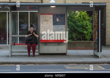 Eine größere Dame für ein Bus an einer Bushaltestelle in Central London mit Handy oder Mobile Smartphone in eine Text- oder eine E-Mail senden oder empfangen. Bus warten. Stockfoto