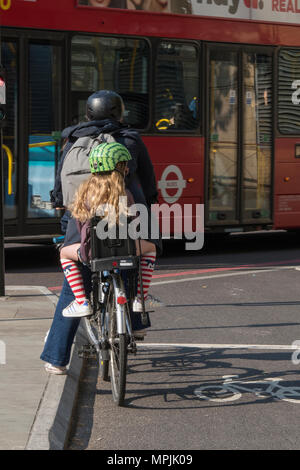 Ein junges Mädchen oder ein Kind in einen Kindersitz auf der Rückseite ein Fahrrad mit Mama reiten durch schwere Staus und Verkehrsbehinderungen im Londoner Schule laufen Stockfoto