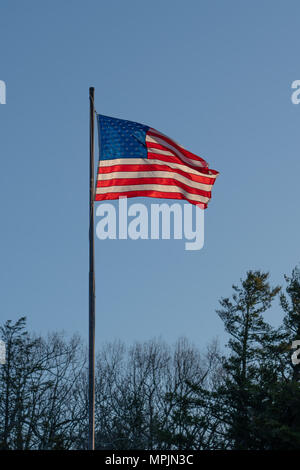 Am frühen Morgen Sonne durch die amerikanische Flagge auf einer Stange mit einem Post dawn blue sky Stockfoto