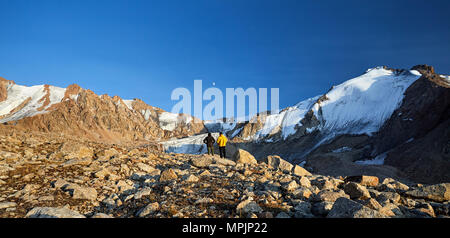 Wanderer in gelb und dunkel Jacken auf Steine, vor der hohen schneebedeckten Berge bei Mondaufgang Hintergrund Stockfoto