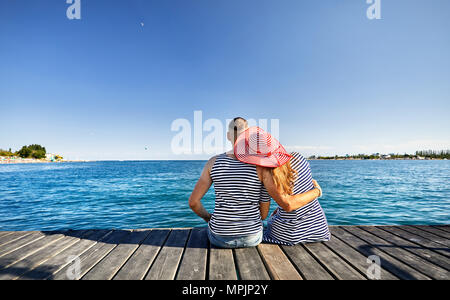 Romantisches Paar in gestreiften Kleid sitzt auf Pier und Suchen im Blue Lake Issyk Kul in Kirgisistan Stockfoto