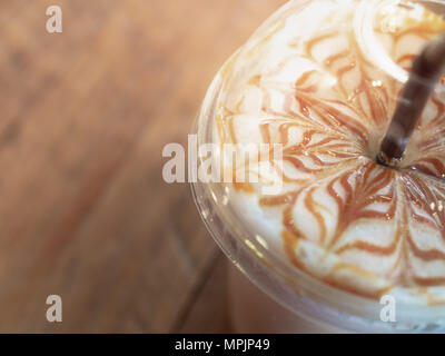 Close-up Iced Caramel Macchiato mit braunen Stroh in mit nach Hause nehmen, Kunststoff, Glas auf Holz- Hintergrund Stockfoto