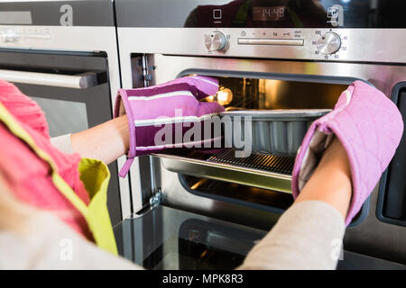Frau setzen Kuchen in den Backofen in der Küche Stockfoto