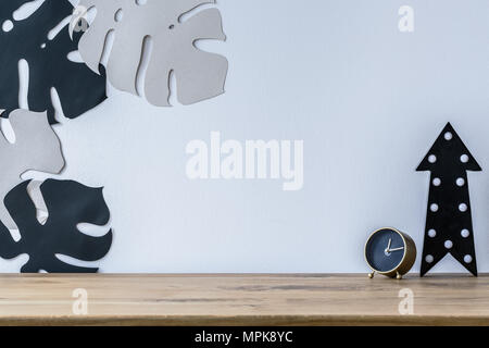 Gold Uhr und der schwarze Pfeil auf hölzernen Schreibtisch gegen weiße Wand mit monstera Blätter im Arbeitsbereich innen Stockfoto