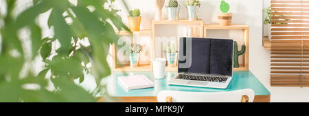 Grüne Pflanze in Unscharfer Vordergrund auf dem Foto von einem Computer für die Arbeit an kleinen Schreibtisch mit Kalender und Kaffee Tasse platziert Stockfoto