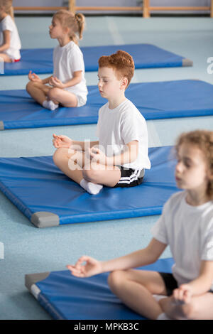 Grundschule Schüler und andere Kinder sitzen auf Matten mit gekreuzten Beinen und Augen in entspannenden Meditation Klasse geschlossen Stockfoto