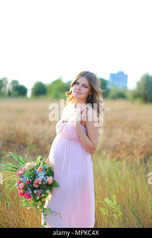 Schwangere Frau tragen rosa Kleid mit Blumenstrauß in Steppen Hintergrund stehen. Stockfoto