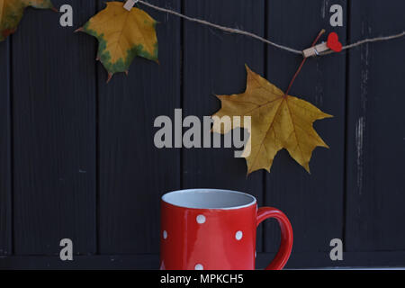 Tasse mit Kaffee auf einem schwarzen Zaun und Blätter im Herbst Stockfoto