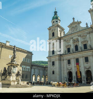 Der barocke Salzburger Dom vom Domplatz aus gesehen. Pferde und Kutschen warten darauf, Touristen für eine Stadtrundfahrt zu nehmen. Stockfoto