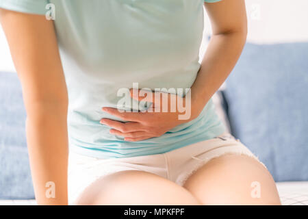 Junge Frau mit Bauchschmerzen beim Sitzen auf dem Sofa und Gefühl stomachache, Symptom der PMS Stockfoto