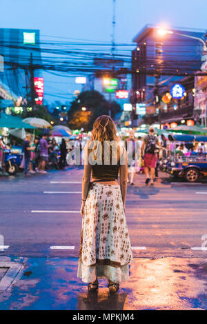 Thailand, Bangkok, junge Frau, die in der Stadt auf der Straße bei Nacht Stockfoto