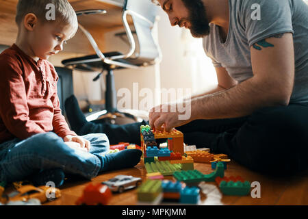 Vater spielen mit Bauklötzen auf dem Boden, während seine traurigen kleinen Sohn aufpassen Stockfoto