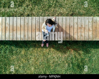 Junge Frau sitzt auf der Promenade Kontrolle ihr Smartphone Stockfoto