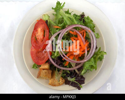 Kleine Salat Salat auf einem weissen Teller, geriebene Karotten, Zwiebeln, Tomaten und Croutons auf einem weißen Tischset Stockfoto