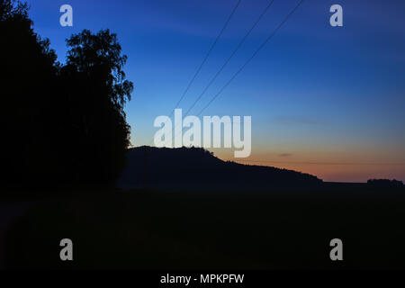 Sonnenuntergang - Landschaft mit Bäumen und Feld und mit Hochspannung Kabel. Stockfoto