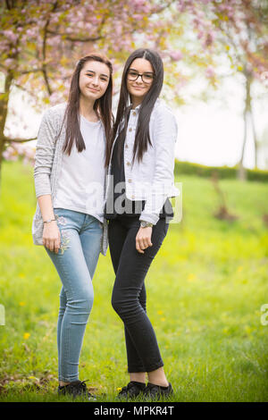 Zwei hübsche Schwestern Mädchen sich gemeinsam amüsiert, das Tragen modischer Kleidung, positive Emotionen. Mädchen auf der Suche an Kamera Stockfoto