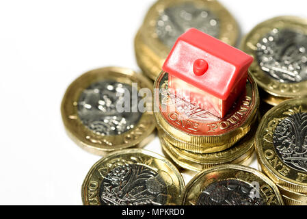 Makro Nahaufnahme eines kleinen Hauses ruht auf neue Pfund Münzen mit einem weißen Hintergrund. Stockfoto