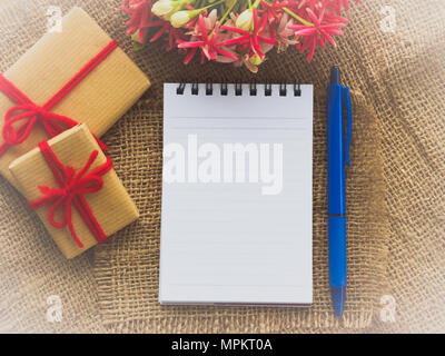 Blumenstrauß, Geschenk und rote Blume, Notenbuch und blauen Stift auf braunen sack Hintergrund Stockfoto