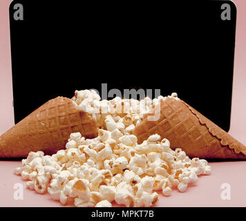 Popcorn mit digitalen Tablet auf rosa Hintergrund. Stockfoto