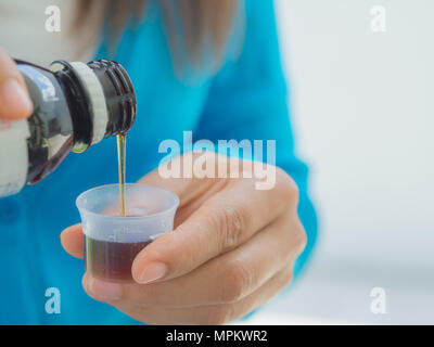 Gesundheitswesen, Menschen und Medizin Konzept - Frau gießen Medikation oder antipyretische Sirup von der Flasche zum Becher Stockfoto