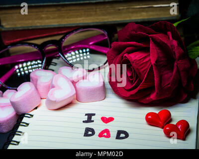 Vatertag Konzept. Ich liebe Papa Nachricht schreiben auf Notiz Buch mit roter Rose, Stapel Bücher, Gläser und süße Marshmallow in der Form von Herzen auf dar Stockfoto