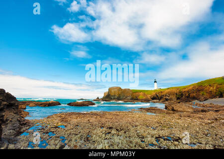 Newport, Oregon, USA - 25. Mai 2016: Querformat mit Big Sky für Copyspace der Yaquina Head Lighthouse aus Kopfsteinpflaster Strand als Menschen Gezeitentümpel erkunden Stockfoto