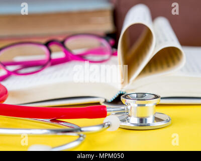 Stapel Bücher, Gläser und ein Stethoskop mit einem Buch in Herzform auf gelb Tabelle Hintergrund Stockfoto