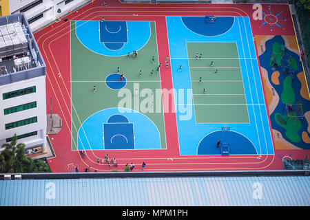 Aus der Vogelperspektive von Grundschulkindern in grüner Uniform, die um die farbenfrohe Freiluft-Ministadionanlage laufen. Singapur. Stockfoto