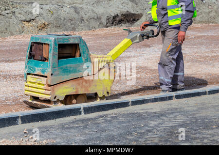 Arbeitnehmer mit rüttelplatte Verdichten des Bodens in einem Stadtpark, Gehweg Wiederaufbau. Stockfoto