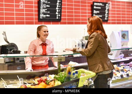 Junge Verkäuferin an der frischen Zähler im Supermarkt serviert eine Kunden - Verkauf von Käse und Fleisch Stockfoto