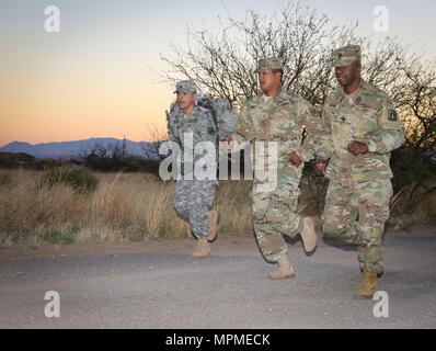 Command Sgt. Maj. Ronnie Bauer (rechts), command Sergeant Major für die 335.- Signal (Theater) und Sgt. Matthew James (Mitte), ein Spezialist für die 98Th Expeditionary Signal Bataillon zugeordnet, 335 SC (T), das neben der Armee finden Spc. Josue Mendez, einem IT-Spezialisten aus dem 319 Expeditionary Signal Bataillon, 335 SC (T), wie Mendez nähert sich die Ziellinie eines zeitgesteuerten 10 Kilometer ruck März mit einer 35-lbs-Pack auf dem Rücken 30. März als Teil des Befehls besten Krieger Wettbewerb 2017 in Fort Huachuca, Arizona gehalten wird. (Offizielle US-Armee Stockfoto