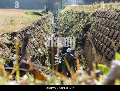 SASEBO, Japan (30. März 2017) Tsunemasa Fujisawa, Marine Engineering Befehl Fernost zugewiesen, führt Chief Utilitiesman Georgios Georgiadis, Naval Mobile Konstruktion Bataillon 5 zugewiesen, und Leutnant Liwei Chen, zu NAVFAC Fernost zugewiesen, durch einen Entwässerungsgraben, Grabsteine, die von der Umgebung auf Hario Shima Ordnance Facility onboard KFBS am 30. März 2017 fiel erholen. Die Grabsteine wurden zurückgewonnen und in einer stabilen Position zurücksetzen. (U.S. Marine Foto von Mass Communication Specialist Seaman Geoffrey S. Barham/Freigegeben) Stockfoto