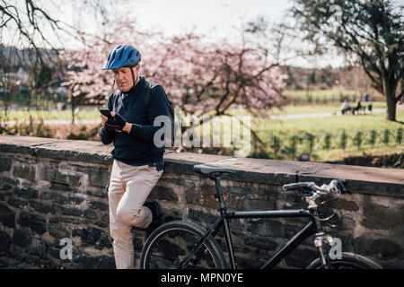 Älterer Mann mit Radfahren mit Smartphone Helm Stockfoto