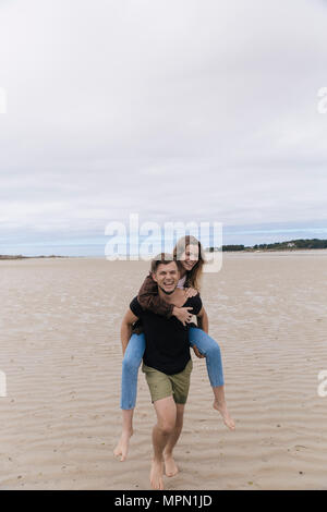 Frankreich, Bretagne, Guisseny, glückliche junge Mann, Freundin Huckepack am Strand Stockfoto