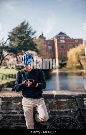 Älterer Mann mit Radfahren mit Smartphone Helm Stockfoto