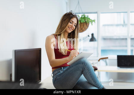 Lächelnd casual junge Frau Notizen im Büro Stockfoto