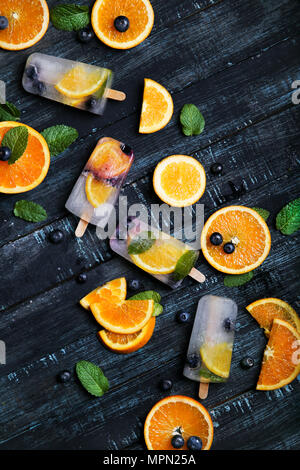 Hausgemachte detox Eis am Stiel mit Blaubeeren, Orangenscheiben und Minze auf schwarzem Holz Stockfoto