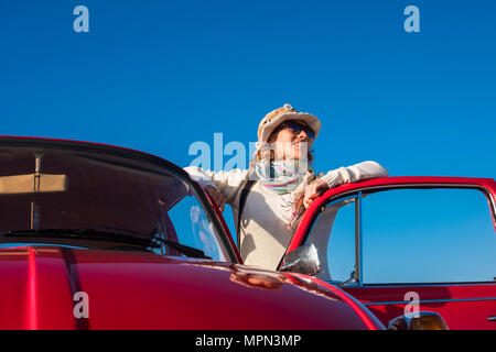 40 s Frau hippy Stil genießen das Wetter draußen von ihrem alten roten Auto. Vintage Leben und Stil, blau klar Himmel Hintergrund Stockfoto