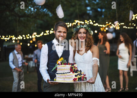 Braut und Bräutigam ein Kuchen Hochzeit außerhalb Holding im Hinterhof. Stockfoto